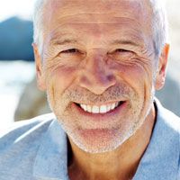 An older man smiles after having a full-mouth reconstruction